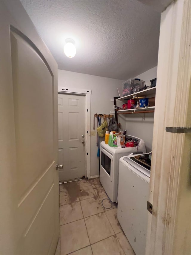 clothes washing area with washer and dryer, light tile patterned floors, and a textured ceiling