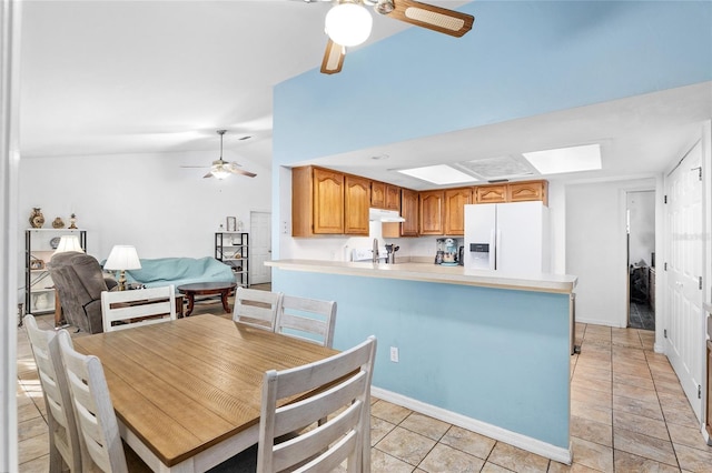 tiled dining area with ceiling fan and vaulted ceiling with skylight