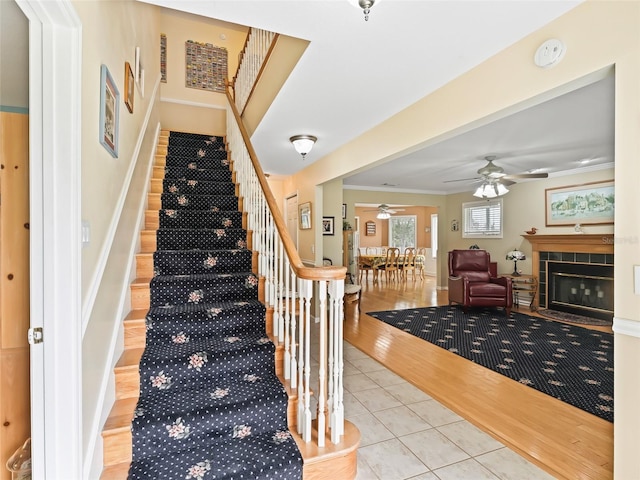 stairway featuring tile patterned flooring, crown molding, ceiling fan, and a tile fireplace