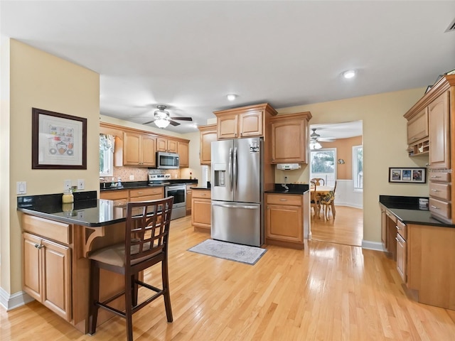 kitchen with tasteful backsplash, a kitchen bar, kitchen peninsula, stainless steel appliances, and light wood-type flooring