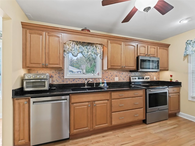 kitchen with dark stone countertops, sink, stainless steel appliances, and light hardwood / wood-style floors