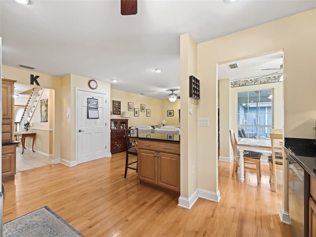 kitchen featuring ceiling fan, stainless steel dishwasher, light hardwood / wood-style floors, and a breakfast bar area