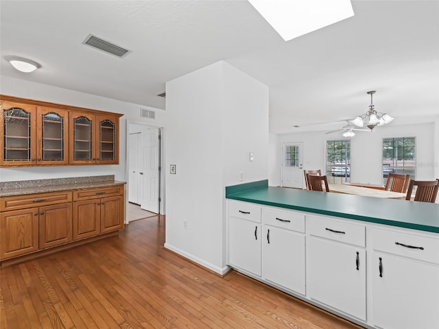 kitchen featuring light hardwood / wood-style flooring, hanging light fixtures, white cabinetry, and a skylight