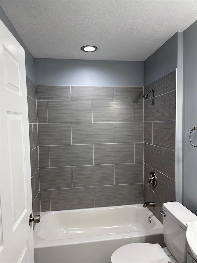 bathroom featuring tiled shower / bath, toilet, and a textured ceiling