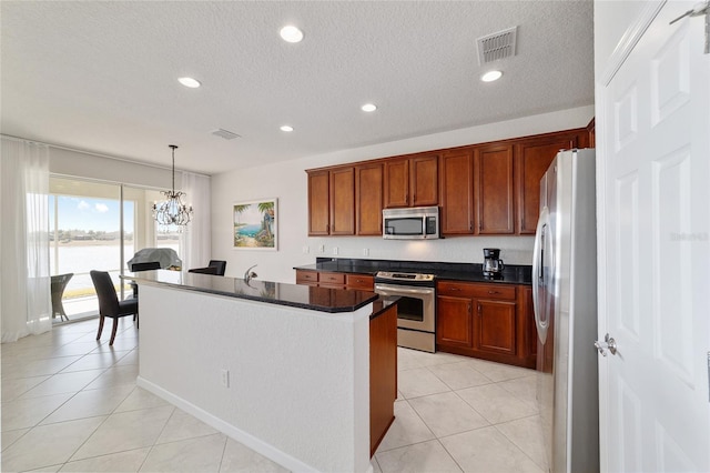 kitchen with pendant lighting, a kitchen island with sink, light tile patterned floors, stainless steel appliances, and an inviting chandelier