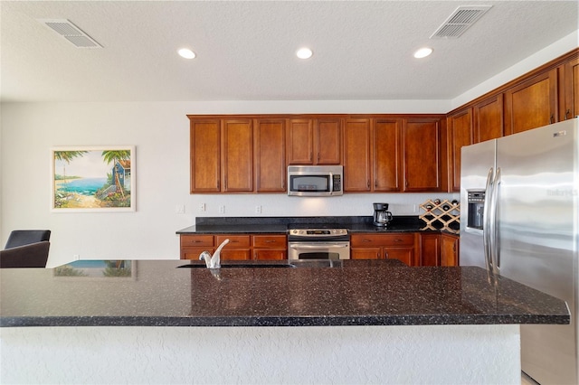 kitchen with an island with sink, appliances with stainless steel finishes, sink, and dark stone countertops