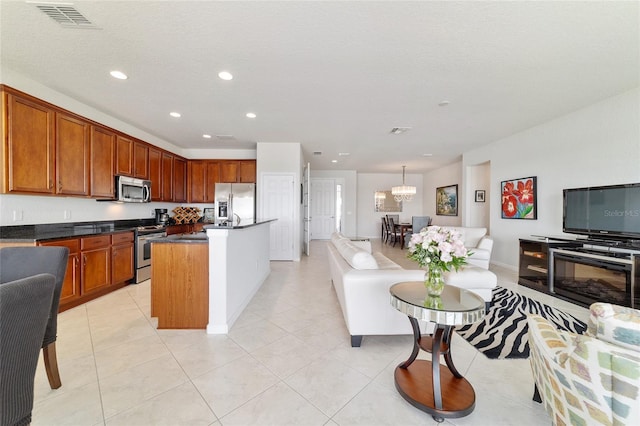 kitchen featuring appliances with stainless steel finishes, pendant lighting, a kitchen island with sink, light tile patterned floors, and a textured ceiling