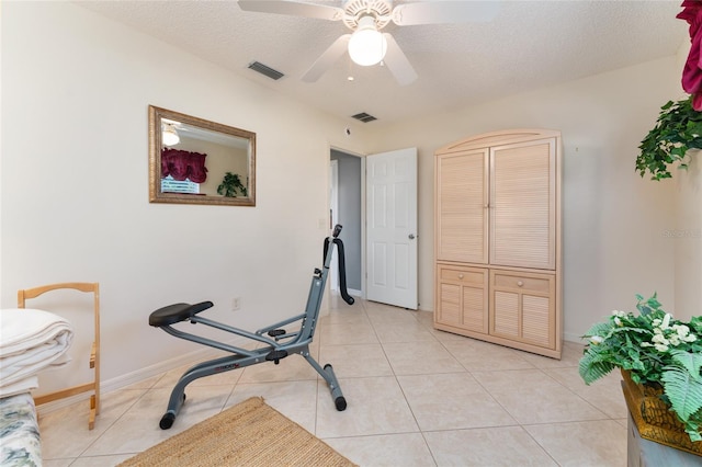 exercise room with light tile patterned flooring, ceiling fan, and a textured ceiling