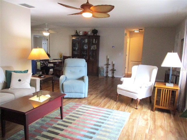 living room with a ceiling fan, visible vents, and wood finished floors