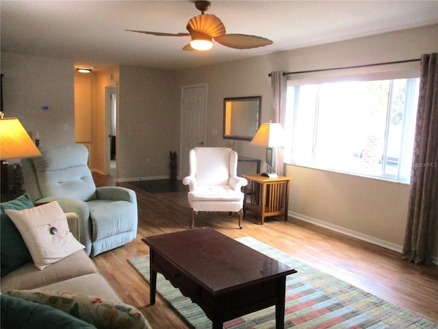 living area featuring a ceiling fan, light wood-type flooring, and baseboards