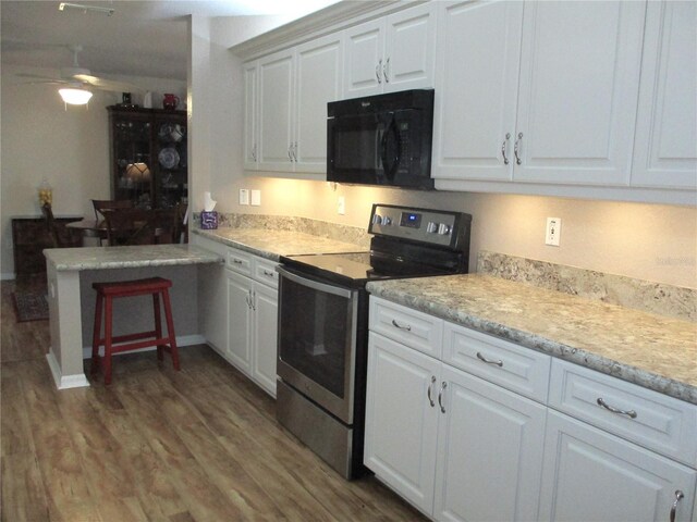 kitchen with black microwave, electric stove, wood finished floors, a peninsula, and white cabinetry