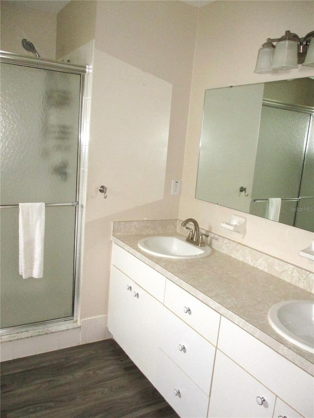 bathroom with double vanity, a shower stall, a sink, and wood finished floors