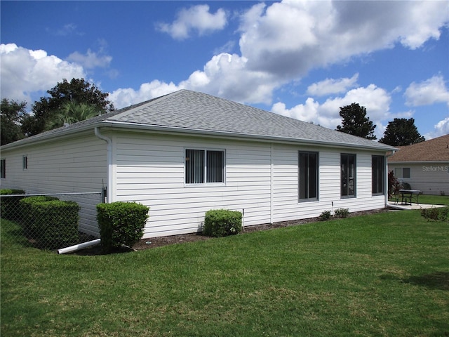 view of side of property featuring roof with shingles, a lawn, and fence