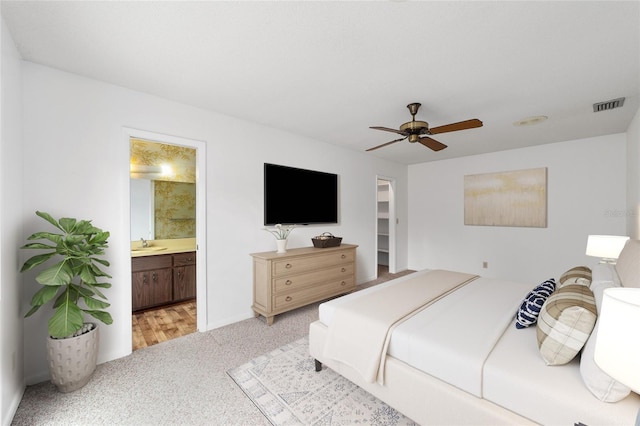 bedroom featuring connected bathroom, light colored carpet, sink, and ceiling fan