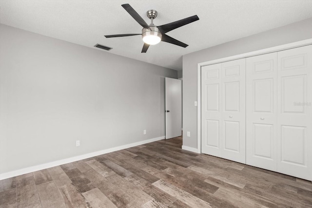 unfurnished bedroom with dark wood-type flooring, a textured ceiling, ceiling fan, and a closet