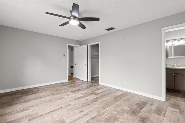 unfurnished bedroom with ensuite bathroom, a spacious closet, ceiling fan, a textured ceiling, and a closet