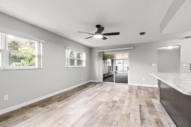 empty room with ceiling fan, plenty of natural light, a textured ceiling, and light wood-type flooring