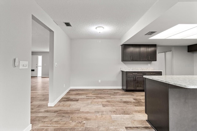 kitchen featuring dark brown cabinetry, light hardwood / wood-style floors, and a textured ceiling