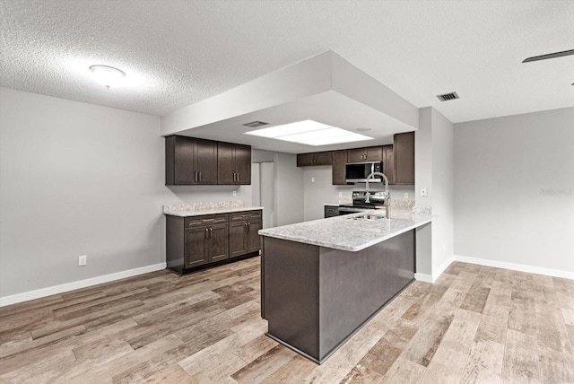 kitchen with light hardwood / wood-style flooring, a breakfast bar, dark brown cabinets, a textured ceiling, and kitchen peninsula