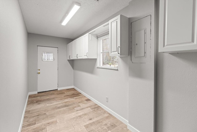 laundry room with light wood-type flooring, electric panel, and a textured ceiling