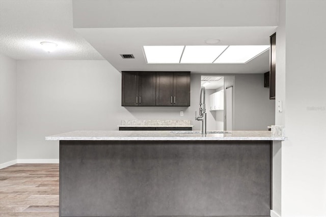 kitchen with dark brown cabinetry, sink, a textured ceiling, light wood-type flooring, and kitchen peninsula