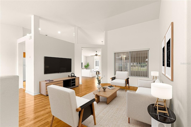 living room with ceiling fan, a high ceiling, and light wood-type flooring