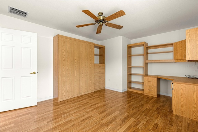 unfurnished office with ceiling fan, built in desk, and hardwood / wood-style floors