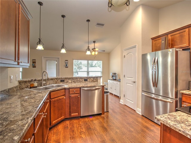 kitchen featuring pendant lighting, sink, dark stone countertops, stainless steel appliances, and dark hardwood / wood-style floors