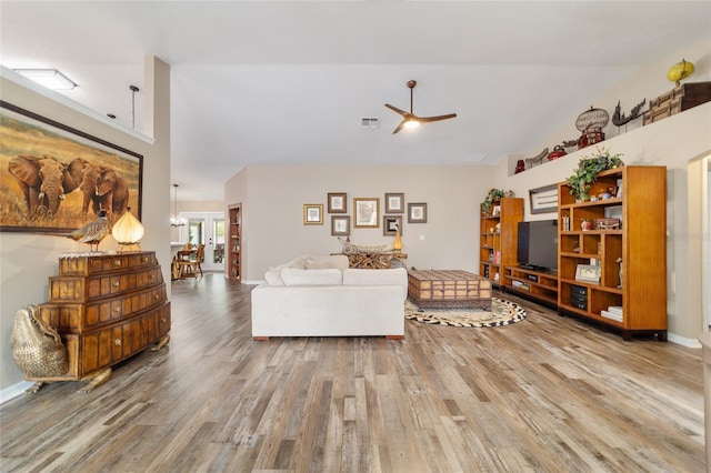 living room featuring ceiling fan with notable chandelier, wood-type flooring, and vaulted ceiling