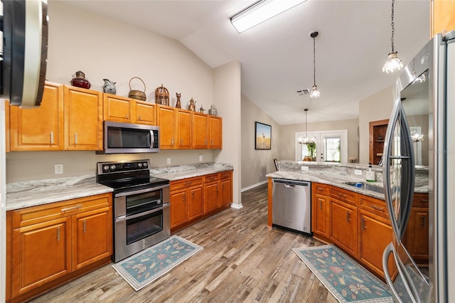 kitchen featuring lofted ceiling, light hardwood / wood-style flooring, appliances with stainless steel finishes, hanging light fixtures, and light stone counters