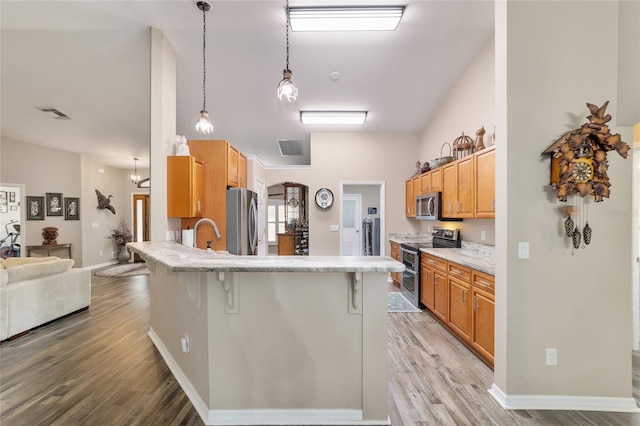 kitchen featuring sink, a breakfast bar area, hanging light fixtures, stainless steel appliances, and light hardwood / wood-style flooring