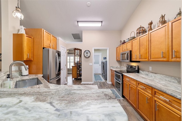 kitchen with sink, light stone counters, hanging light fixtures, light hardwood / wood-style flooring, and stainless steel appliances