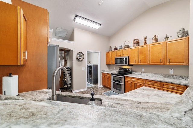 kitchen with vaulted ceiling, appliances with stainless steel finishes, sink, light stone countertops, and light wood-type flooring