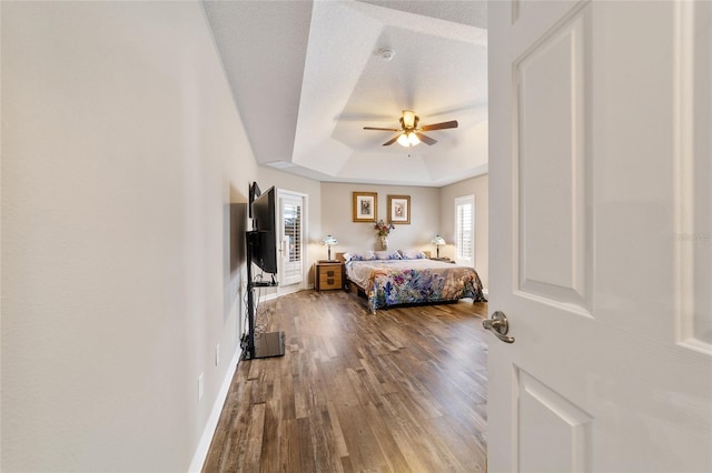 bedroom with ceiling fan, a raised ceiling, hardwood / wood-style floors, and a textured ceiling