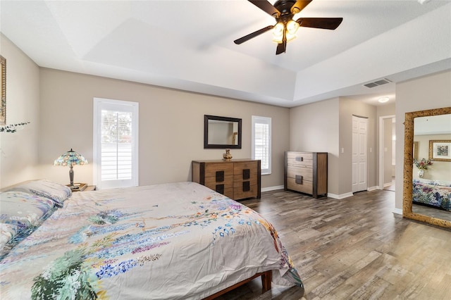 bedroom with a raised ceiling, dark hardwood / wood-style floors, ceiling fan, and a closet