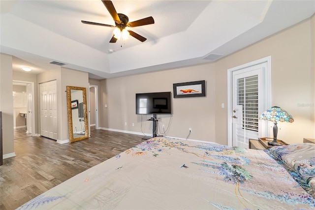 bedroom with ceiling fan, a tray ceiling, and dark hardwood / wood-style flooring