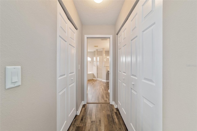 corridor with a textured ceiling and dark hardwood / wood-style flooring