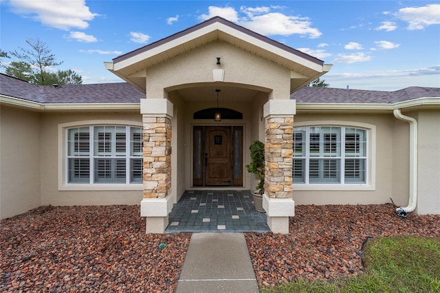 entrance to property featuring a shingled roof, stone siding, and stucco siding