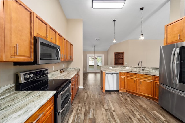 kitchen featuring brown cabinetry, appliances with stainless steel finishes, wood finished floors, a peninsula, and a sink