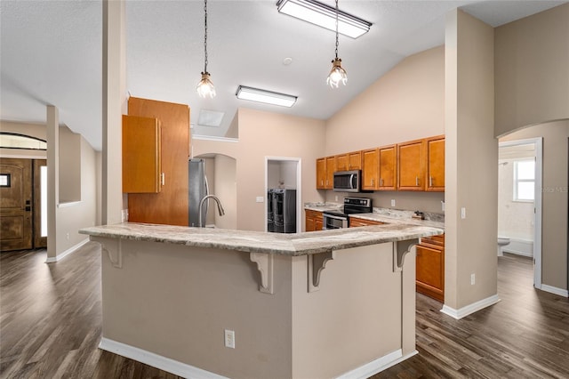 kitchen featuring arched walkways, brown cabinetry, a kitchen breakfast bar, stainless steel appliances, and light countertops