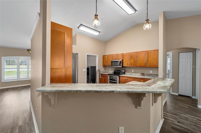 kitchen featuring arched walkways, stainless steel appliances, a peninsula, dark wood-style flooring, and brown cabinetry