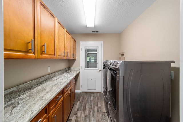 laundry area featuring cabinet space, visible vents, dark wood-style flooring, washing machine and clothes dryer, and a textured ceiling