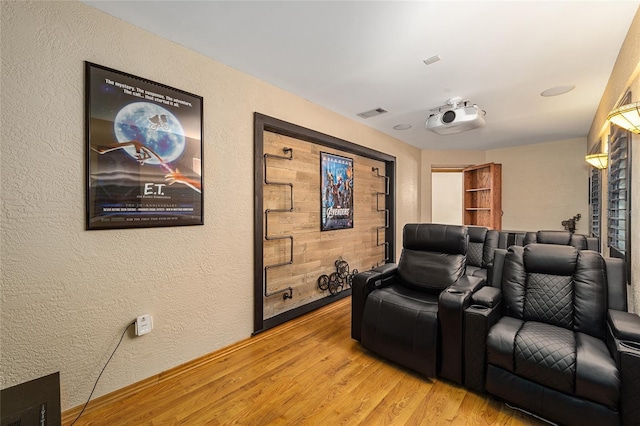 cinema room featuring light wood-style floors, visible vents, and a textured wall