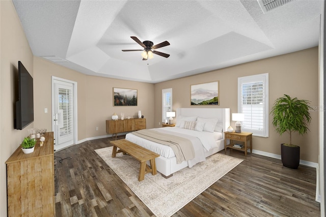 bedroom featuring access to exterior, a raised ceiling, multiple windows, and dark wood-style floors