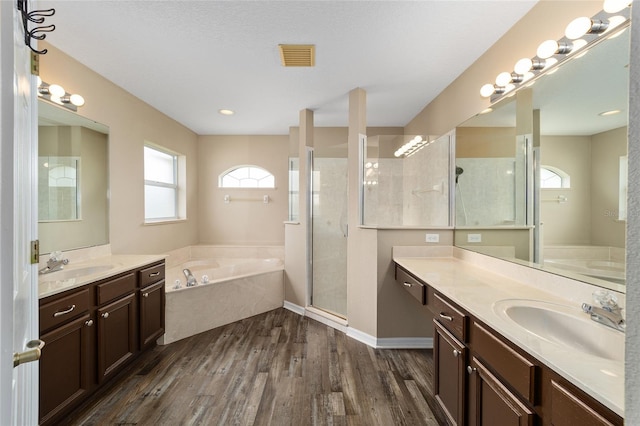 bathroom featuring a bath, a shower stall, a sink, and wood finished floors