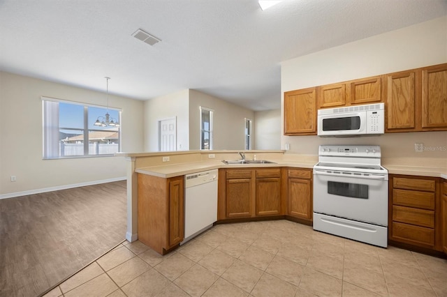 kitchen with sink, white appliances, hanging light fixtures, kitchen peninsula, and a chandelier