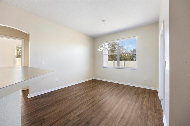 unfurnished dining area featuring dark hardwood / wood-style flooring, a healthy amount of sunlight, and an inviting chandelier