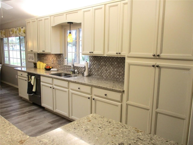 kitchen with black dishwasher, decorative backsplash, cream cabinets, a sink, and light stone countertops