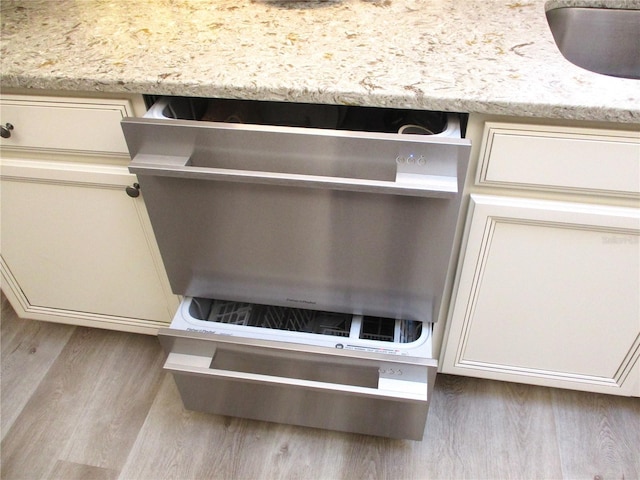 interior details with cream cabinetry, a sink, light wood finished floors, and light stone countertops