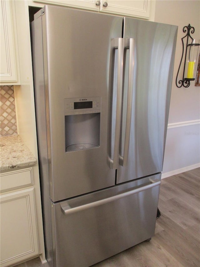 interior details with light stone counters, baseboards, light wood-type flooring, backsplash, and stainless steel fridge with ice dispenser